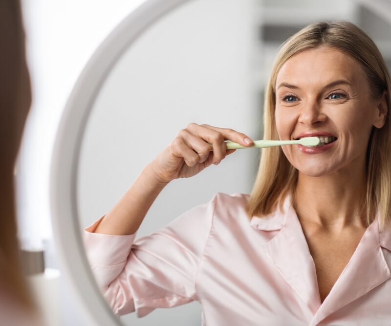 Beautiful Mature Female Brushing Her Teeth With Toothbrush Near Mirror