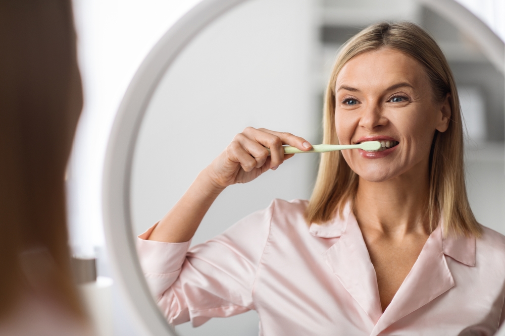 Beautiful Mature Female Brushing Her Teeth With Toothbrush Near Mirror