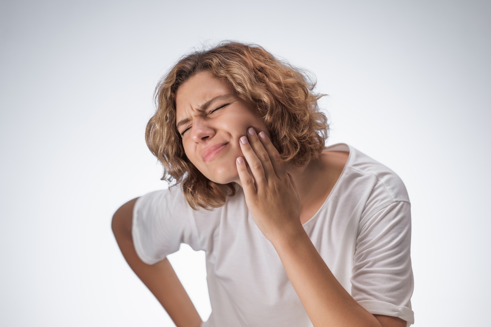 Young woman grimaces in pain while pressing her cheek, showing clear signs of oral discomfort due to tooth or gum issues